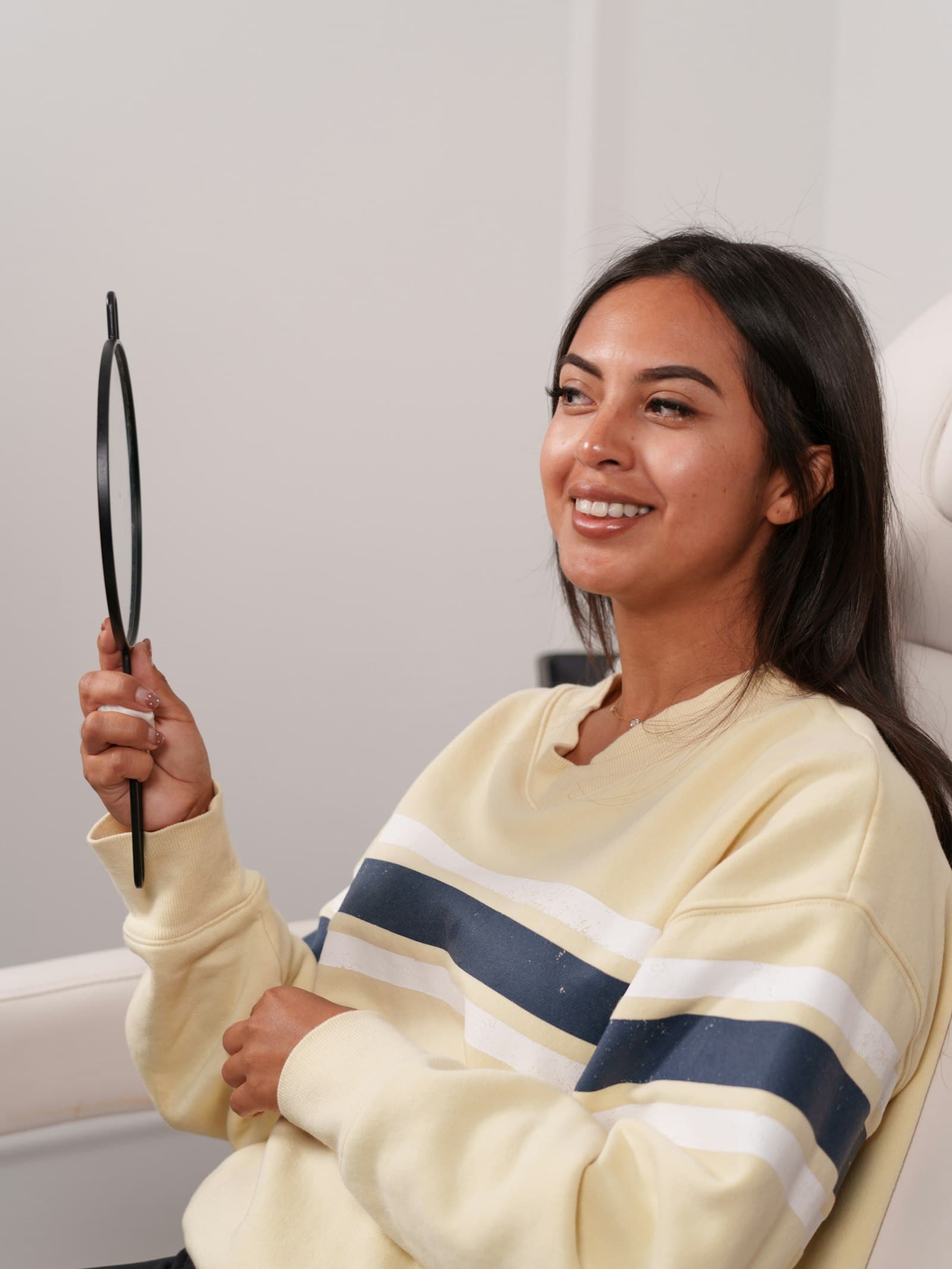 A smiling client in a treatment chair holding a mirror